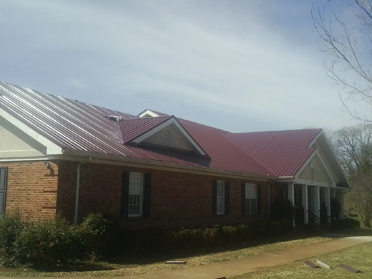 Red metal roof with gabled entries on a long brick building, from a Hail Damage Roof Repair job in Fountain Inn