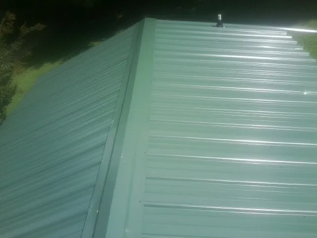 New green metal panels meeting at the ridge of a roof — Flat Roof Repair work by our crew in Fountain Inn