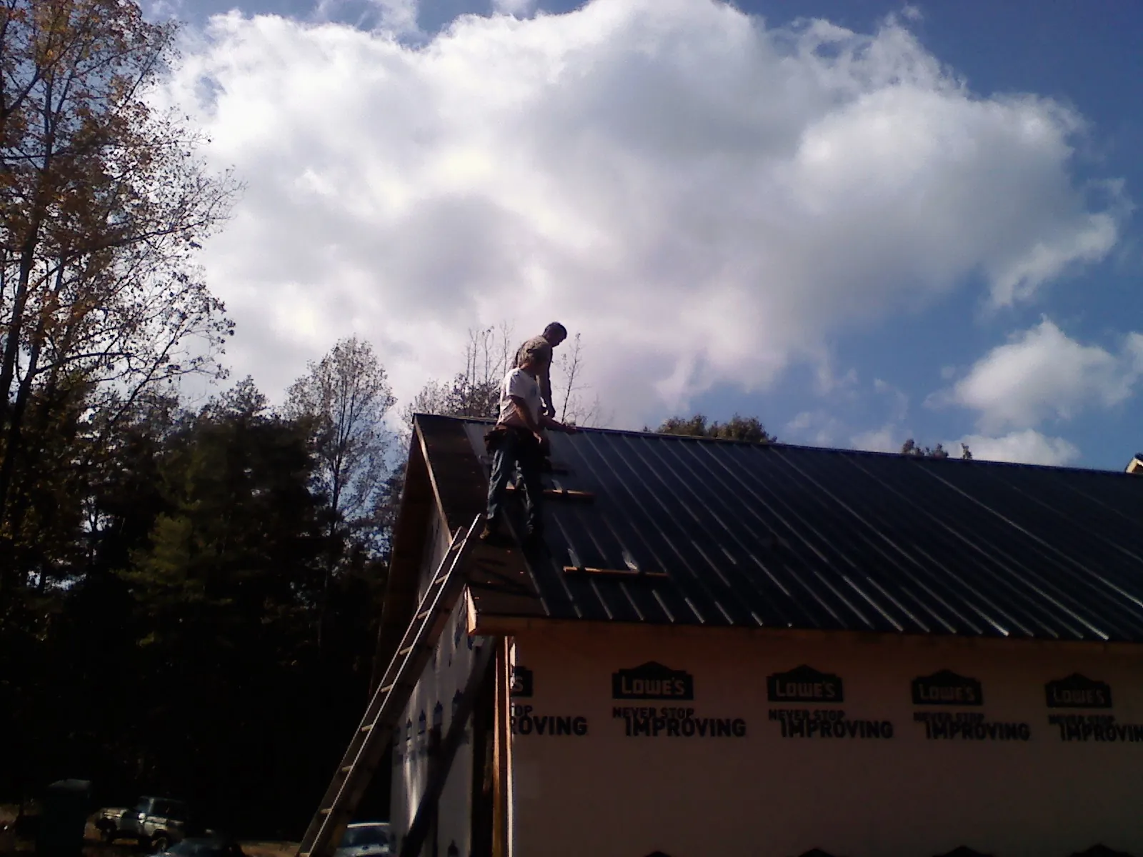 Roofer fastening dark metal panels high against a cloudy sky, from a Roof Inspection job in Fountain Inn