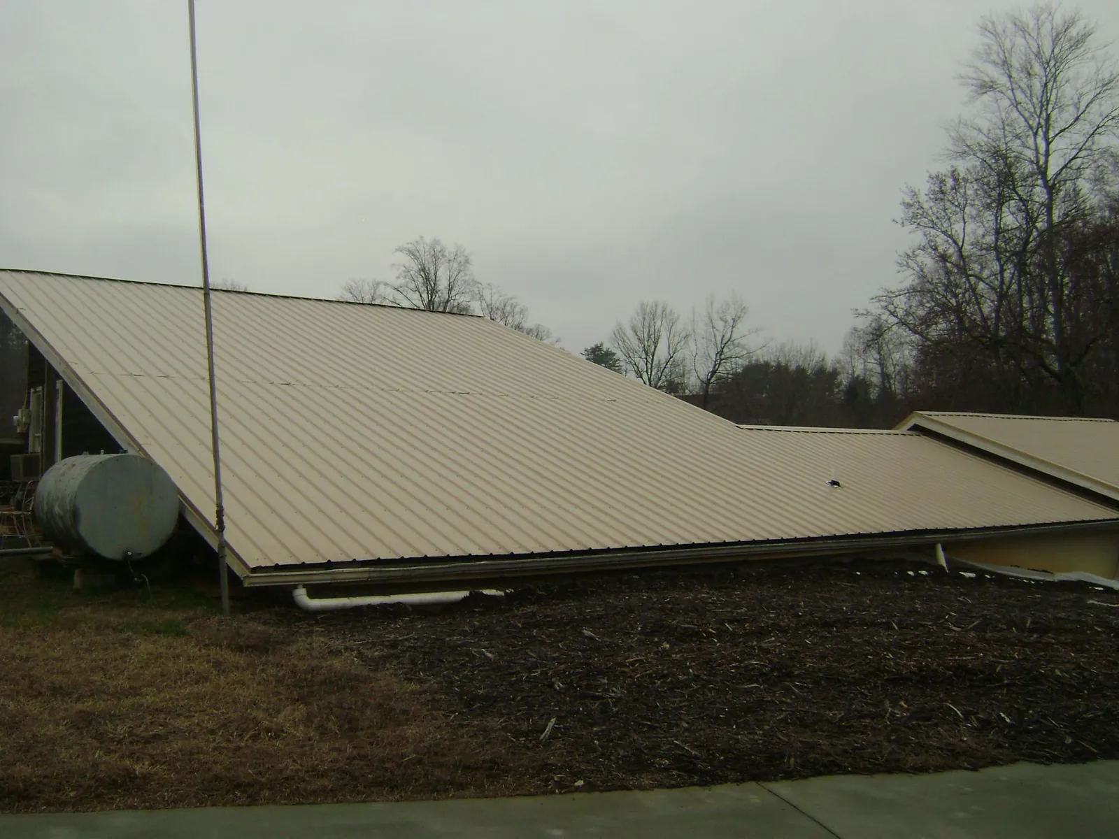 Wide tan metal roof plane seen from the ground beside a propane tank in Fountain Inn