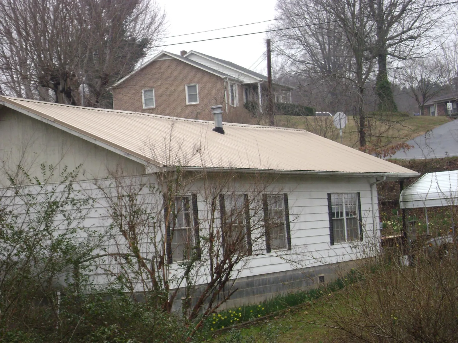 Tan metal roof on a white sided house set into a hillside — Commercial Roofing by Roofing Brothers in Fountain Inn